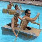 Couples racing cardboard boats in the pool